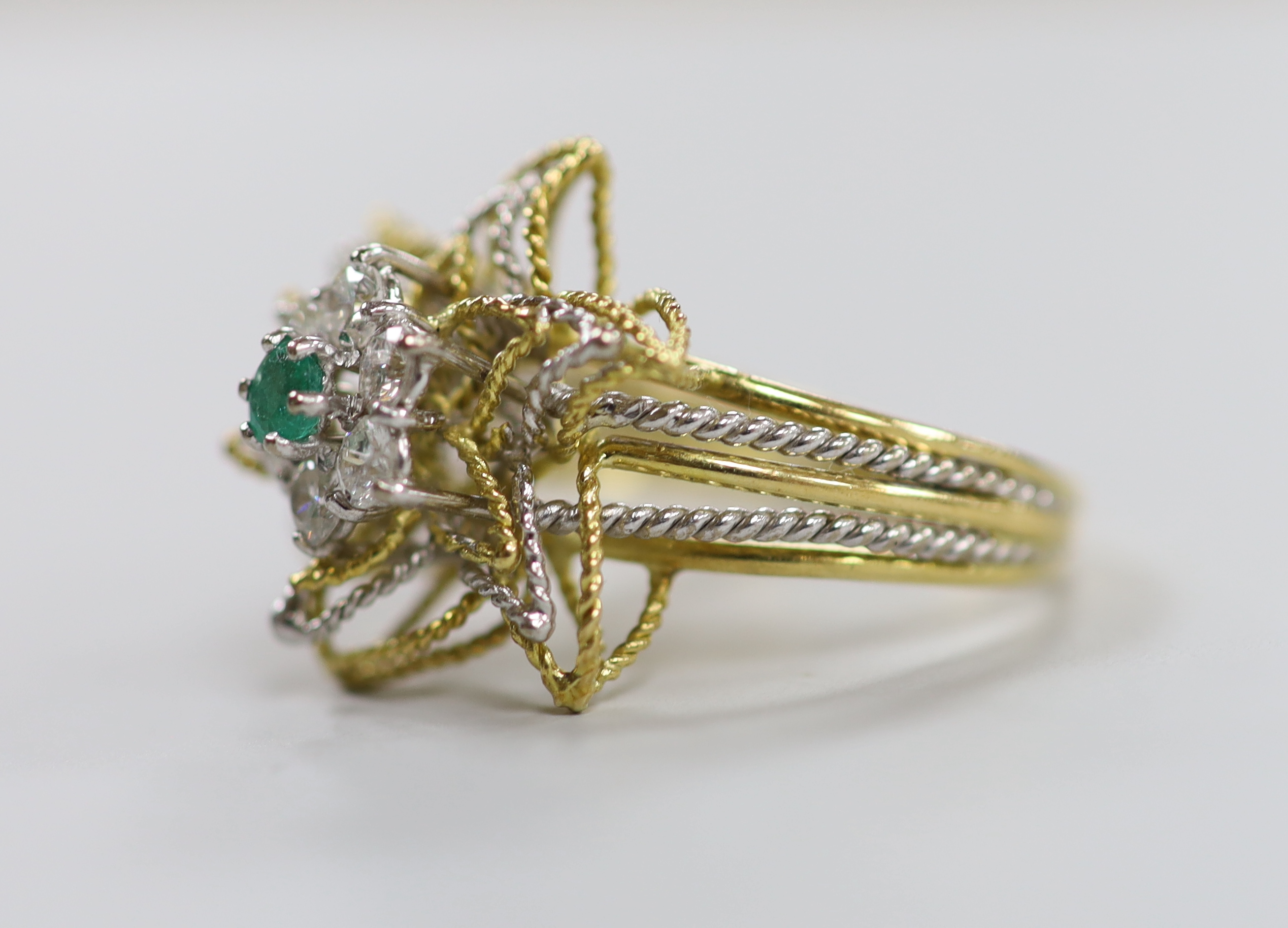 A yellow and white metal, emerald and diamond cluster set stylised flower head ring, size P, gross weight 6.3 grams.